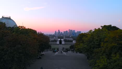 Aerial-Drone-through-Greenwich-Park-over-Statue,-revealing-Canary-Wharf-and-London-Skyline