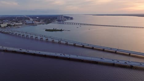 Aerial-wide-shot-showing-traffic-on-Caloosahatchee-and-Edison-bridge-during-sunset-time---Loftons-Island-in-the-middle-of-river---Fort-Myers,-Florida