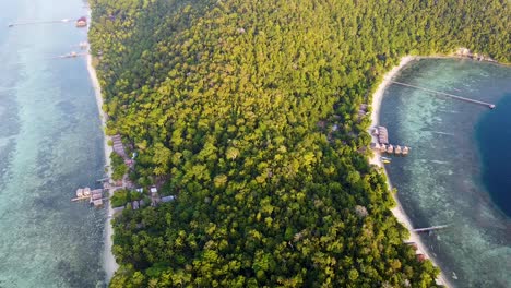 Luftaufnahme-Der-Mit-Dschungelregenwald-Bedeckten-Tropischen-Insellandschaft-Mit-Strandhütten-Am-Wasser-In-Raja-Ampat,-West-Papua,-Indonesien