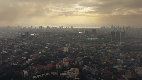 Filmischer-Drohnenflug-über-Die-Stadt-Manila-Und-Silhouette-Eines-Wolkenkratzers,-Beleuchtet-Durch-Sonnenstrahlen-Zwischen-Dunklen-Wolken---Mystischer-Stadtflug-Auf-Den-Philippinen