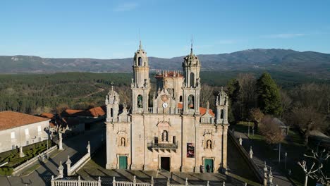Drone-pull-back-from-clock-and-bell-tower-to-reveal-beautiful-grass-lawn-of-gothic-sanctuary-in-Spain