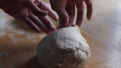 Fresh-dough-ball-being-plucked-by-hands-of-chef-on-wooden-kitchen-tabletop,-filmed-as-closeup-slow-motion-shot