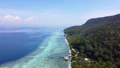 Umgekehrte-Luftaufnahme-Von-Strandhütten-über-Kristallklarem-Meerwasser,-Korallenriffen-Und-Regenwaldbäumen-Auf-Einer-Tropischen-Insel-In-Raja-Ampat,-West-Papua,-Indonesien