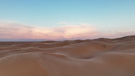 The-drone-is-flying-low-over-the-dunes-of-the-Sahara-desert-with-the-wind-blowing-sand-over-the-dunes-with-the-sun-rising-in-Tunisia-Aerial-Footage-4K