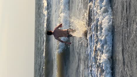Vertikale-Aufnahme-Eines-Jungen-Mannes,-Der-Während-Der-Sommerferien-Ins-Meer-Rennt-Und-Ins-Wasser-Springt