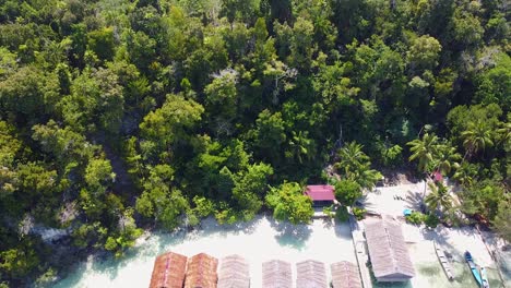 Luftaufnahme-über-Einer-Abgelegenen-Strandhüttenunterkunft-Am-Wasser-Mit-Blick-Auf-Das-Korallenriff-Und-Das-Kristallklare-Meerwasser-In-Raja-Ampat,-West-Papua,-Indonesien