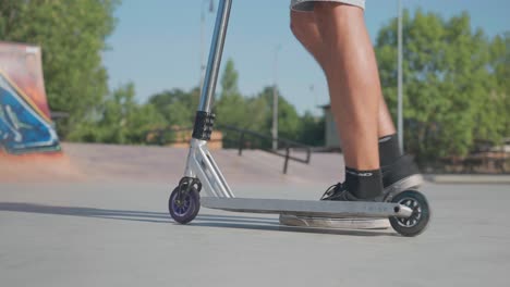 Man-push-stunt-scooter-with-rubber-wheels-and-put-foot-on-deck-at-skatepark