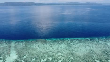 Aerial-flying-over-exotic-tropical-crystal-clear-waters-with-coral-reef-and-deep-blue-ocean-in-Raja-Ampat,-West-Papua,-Indonesia