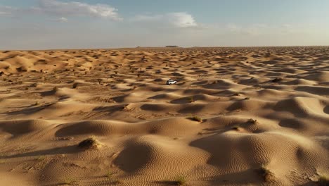 The-drone-is-flying-forward-looking-at-a-white-car-driving-through-the-Sahara-desert-in-Tunisia-Aerial-Footage-4K