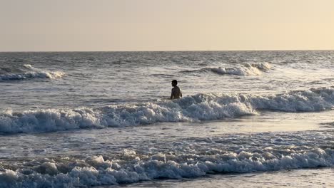 Young-man-playing-with-the-waves-in-the-sea-during-sunset