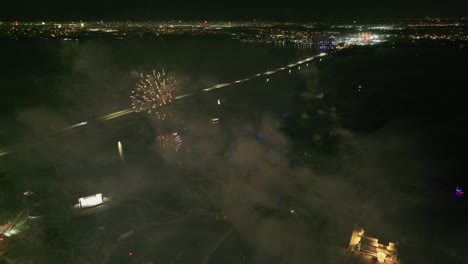 Drone-flight-over-glowing-fireworks-at-dark-night-sky-and-illuminated-city-of-Fort-Myers,-Florida---Top-down-view