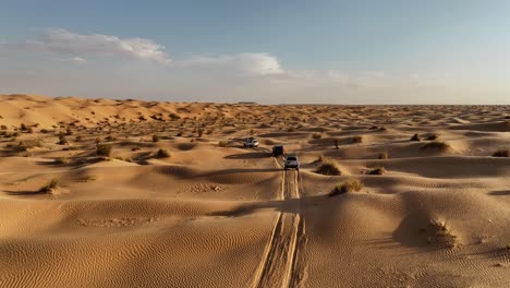 The-drone-is-flying-up-looking-at-three-cars-driving-through-the-Sahara-desert-in-Tunisia-Aerial-Footage-4K
