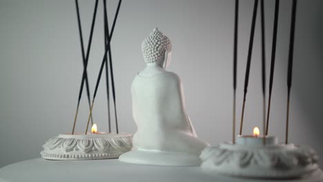 Close-up-shot-of-a-buddha's-mini-statue-placed-between-rotating-incense-sticks-and-candles