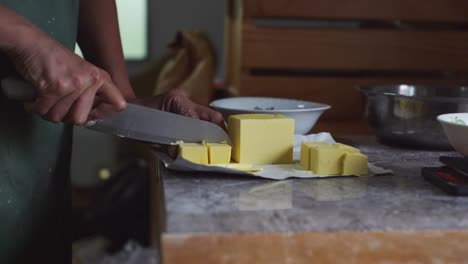 Hard-stick-of-butter-being-cut-to-smaller-cubes,-filmed-as-medium-close-up-slow-motion-shot