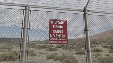 High-quality-3D-CGI-render-with-a-smooth-dollying-out-shot-of-a-chainlink-fence-at-a-high-security-installation-in-a-desert-scene,-with-a-Military-Firing-Range-No-Entry-sign