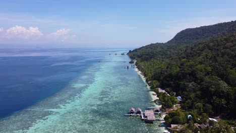 Luftdrohne-Steigt-über-Einer-Strandhüttenunterkunft-Mit-Blick-Auf-Das-Korallenriff-Im-Exotischen-Tauchziel-Raja-Ampat-In-West-Papua,-Indonesien