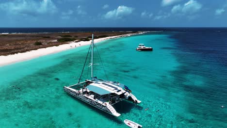 The-drone-is-flying-away-from-a-catamaran-that-is-anchord-near-little-curacao-with-clear-blue-water-and-people-swim-in-Curacao-Aerial-Footage-4K