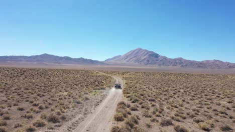 Black-convertible-car-driving-down-a-dirt-road-in-the-Nevada-plains-fading-off-into-the-distance
