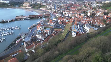 Forward-drone-shot-of-a-crowded-city-of-Scarborough-North-Yorkshire-near-a-sea-with-some-boats-during-daytime-in-England,-UK