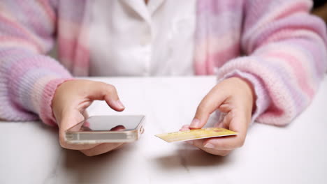 Close-up-woman's-hand-holds-a-smartphone-and-use-a-mockup-Bank-credit-card-for-online-shopping-services-to-pay-money-with-cashless-technology