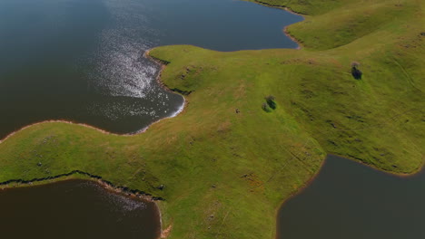 Aerial-reveal-of-lake-surrounded-by-green-hills,-San-Luis-Reservoir-in-California