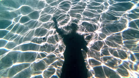 Artistic-underwater-shot-of-a-swimming-person's-silhouette-on-the-ocean-floor