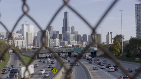 Downtown-Chicago-skyline-and-highway-traffic,-viewed-through-a-fence-in-daylight