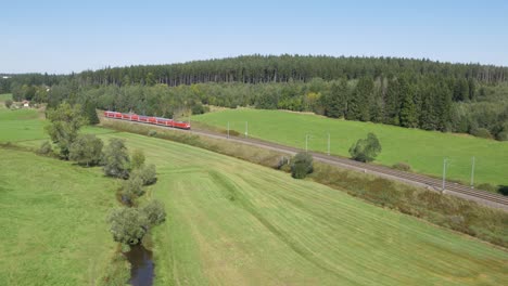 Aerial-shot-of-a-red-DB-train-moving-through-a-lush-green-landscape