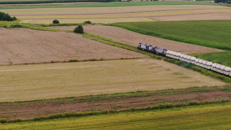 Modern-freight-train-with-industrial-cargo-moves-through-rural-Poland,-aerial-view