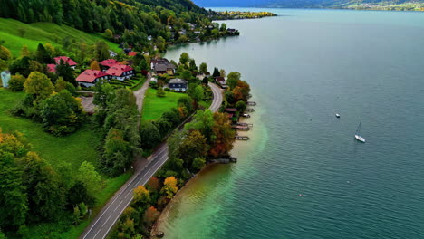 Luftaufnahme-Des-Attersees-In-Österreich-Mit-Häusern-Am-Seeufer,-Umgeben-Von-Herbstlich-Gefärbten-Bäumen-Und-Einem-Segelboot