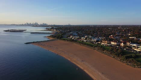 Drone-footage-over-Brighton-Beach,-with-Melbourne's-skyline-in-the-far-horizon