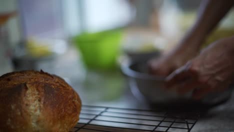 Focus-rack-from-cooked-bread-roll-to-uncooked-dough-being-kneaded-by-hand-in-steel-bowl,-filmed-as-close-up-slow-motion-shot