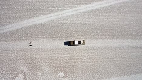 Bird's-View-Truck-Driving-Salar-de-Uyuni-Bolivia,-2-eBikes-Riding-in-Front