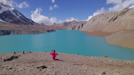 Filmy-drone-shot-reveals-Nepal-landscape-of-Tilicho-World's-highest-Lake,-woman-in-pink-dress-walks-with-Heroine-feels,-cinematic-blue-sky-with-clouds-4K