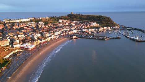 Aerial-parallax-shot-of-and-old-town-with-a-small-hill-beside-the-harbor-with-boats-in-Scarborough-North-Yorkshire,-England-