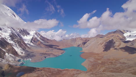 World-Highest-Altitude-Tilicho-Lake-in-Nepal-landscape-of-Annapurna-Mountain-Circuit,-drone-shot-revealing-beautiful-lake-under-the-pleasant-weather,-clouds,-blue-sky,-snow,-and-land-4K
