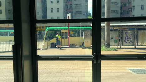 City-bus-stop-filmed-from-behind-a-glass-window-with-people-walking-on-the-sidewalk-in-the-foreground,-Hong-Kong,-China