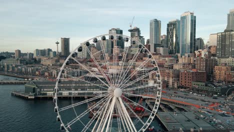 Drone-flyover-above-Seattle-ferris-wheel-to-reveal-dense-urban-buildings-and-skyline-at-sunset