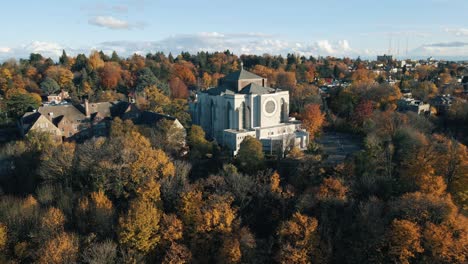 Drone-orbit-pullback-above-beautiful-cathedral-surrounded-by-fire-red-orange-fall-foliage,-Washington