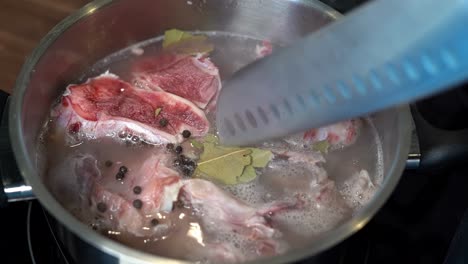 Dried-Bay-Leaves-pushed-down-into-bone-broth-pan-with-knife,-close-up-slow-motion