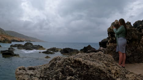 Aufnahme-Einer-Touristin,-Die-An-Einem-Bewölkten-Tag-Wellen-Fotografiert,-Die-Am-Felsigen-Strand-Von-Malta-Entlangbrechen