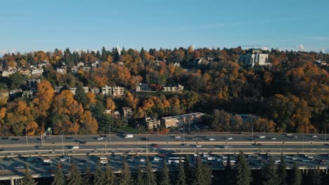 Aerial-pan-across-vibrant-orange-red-fall-colored-trees-lining-traffic-and-busy-highway-in-Seattle-Washington