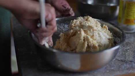 Raw-dough-ingredients-mixed-using-baking-spoon-in-steel-bowl-on-kitchen-tabletop,-filmed-as-closeup-handheld-slow-motion-shot