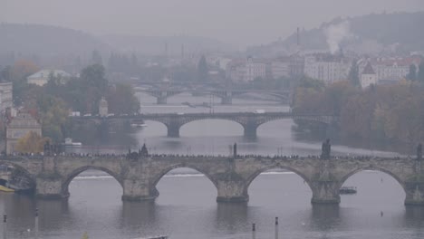 Foggy-view-of-the-Vltava-River-and-Charles-Bridge-in-Prague,-bustling-with-tourists