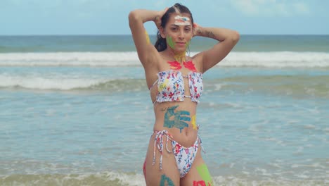 En-El-Caribe,-Una-Chica-Con-Pintura-Corporal-Y-Bikini-Disfruta-Del-Sol-En-Una-Playa-De-Arena-Blanca-Con-Olas-Del-Océano-Al-Fondo