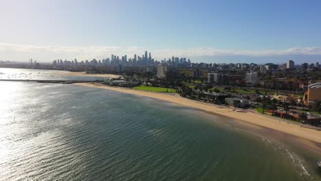 Aerial-footage-over-the-seas-of-St-Kilda-Beach,-with-Melbourne's-CBD-skyline-in-the-horizon-on-a-beautiful-autumn-windy-afternoon