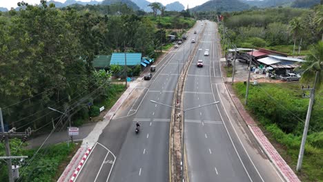 Aerial-op-shot-of-a-girl-riding-a-scooter-in-road-surrounded-by-greenery-in-Thailand