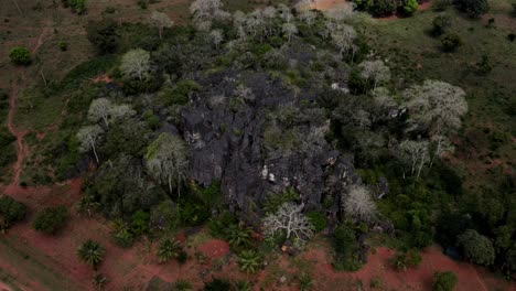Aerial-view-of-a-rock-formation-in-Kenya,-surrounded-by-tropical-plants-and-palm-trees