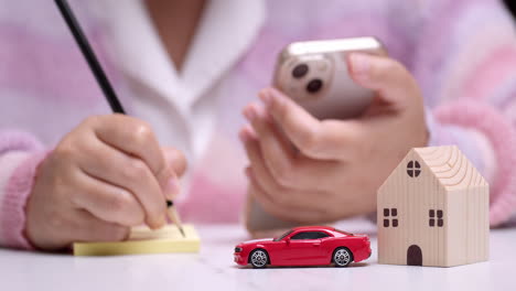 Close-up-of-an-individual-calculating-finances-on-her-car-and-house-loans-using-a-pencil,-paper,-and-a-mobile-phone-as-calculator