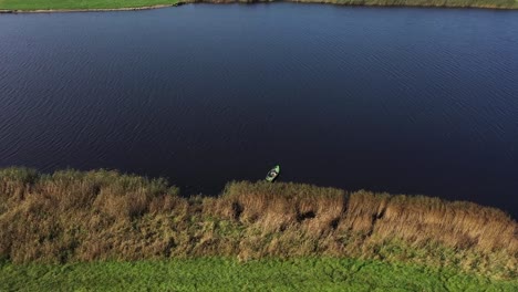 Drone's-Aerial-Sweep:-Capturing-a-River-Scene,-A-Fishing-Boat,-and-a-Fisher-Amidst-Rustling-Reeds